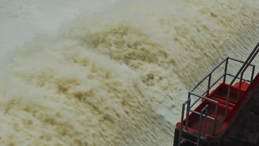 Dam floodgate with rapid water discharge, white splash and strong flow.