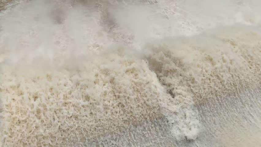Close-up of dam releasing massive white water, foamy splash and roaring flood.