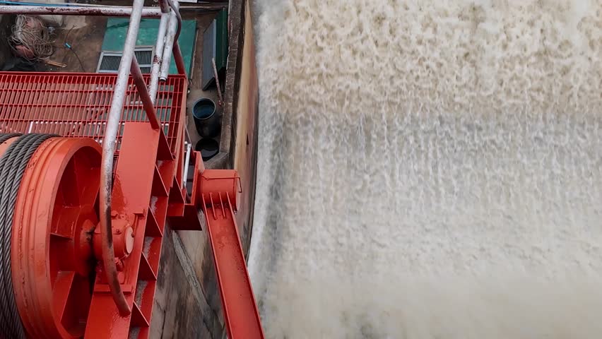 Dam floodgate releasing turbulent water with spray and mist, showing flood discharge power.