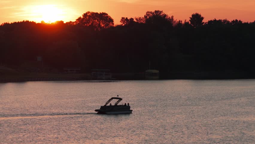 Telephoto dolly aerial shot of a pontoon boat at sunset on North Center Lake in Minnesota. 4K