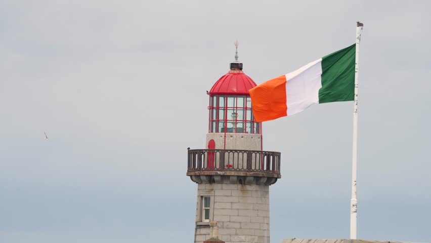 60 fps 4k footage of a lighthouse in a Dublin harbor, Irish flag blowing in the wind on an overcast day.