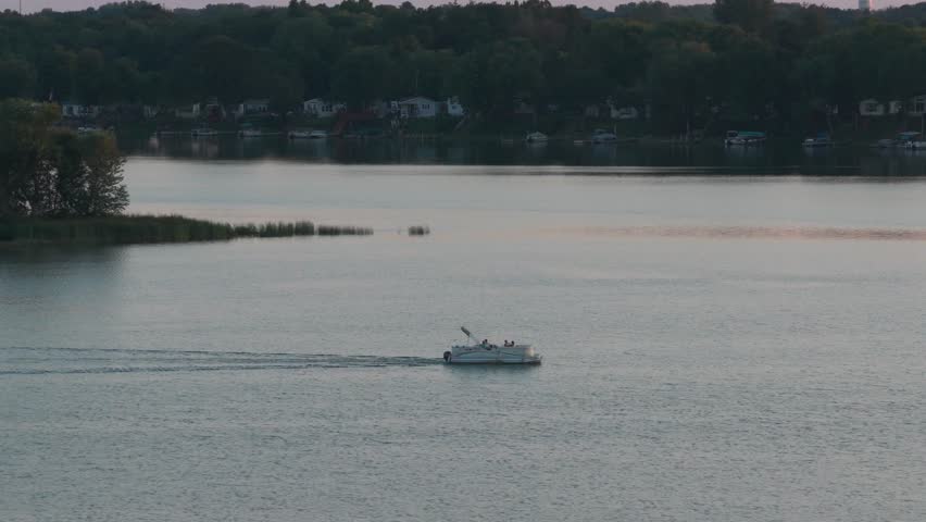 Telephoto aerial dolly shot of a pontoon boat on North Center Lake at sunset in Minnesota. 4K