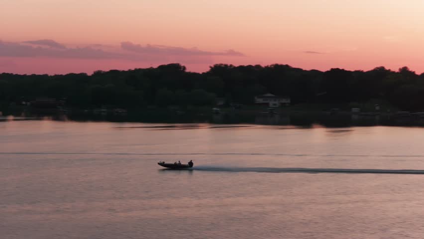 Aerial telephoto dolly shot of a speed boat racing across a lake during sunset in Minnesota. 4K