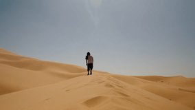 Person walks along the ridge of a golden sand dune in Merzouga, Sahara Desert, under clear midday skies. - Powered by Shutterstock - Get 15% off with code: PIKWIZARD15