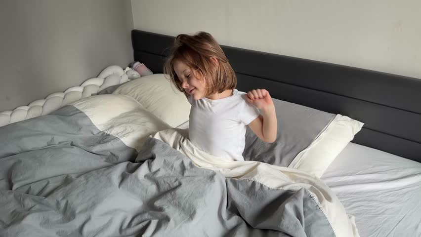 Little girl waking up in her parents bed in a modern apartment. Concept of morning routine, beginning of a new day and peaceful transition from sleep in childhood. High quality 4k footage