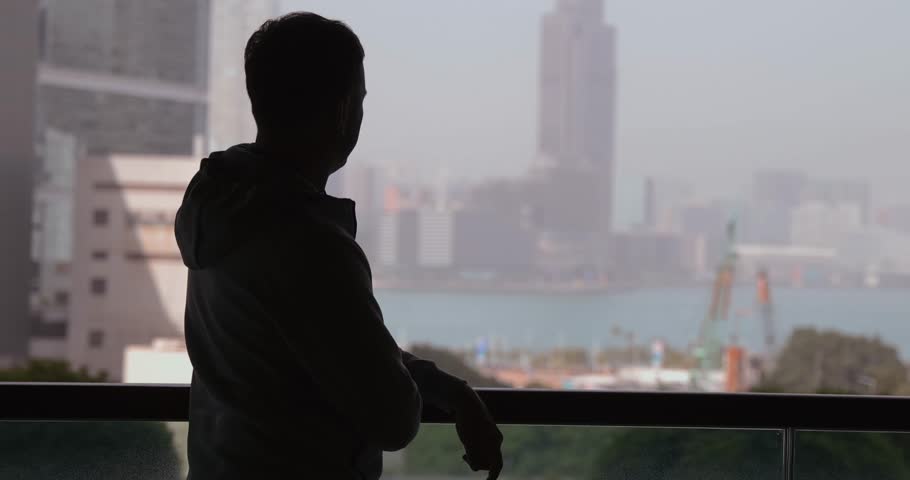 Silhouetted man gazing urban skyline from balcony, reflecting, day, cityscape, waterfront view, contemplative mood, modern architecture.