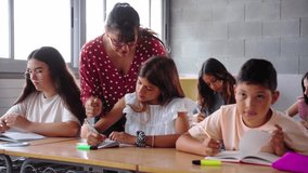 Elementary school teacher assisting students with their schoolwork, guiding a young boy while other children focus on writing in their notebooks at their desks - Powered by Shutterstock - Get 15% off with code: PIKWIZARD15