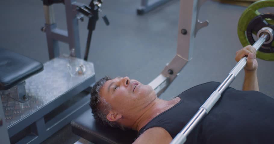 Gym workout. Bench press. Middle aged Caucasian man trains his pectoral muscles in the gym. Middle-aged man focuses on pectoral muscles with bench press exercise at the gym.