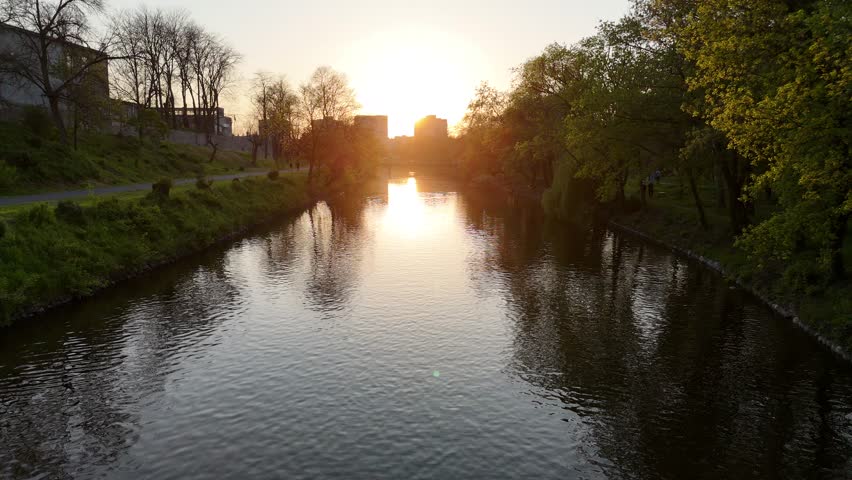 Scenic drone aerial footage of Yambol city park in Bulgaria, showing trees, river, and sunset golden hour light.