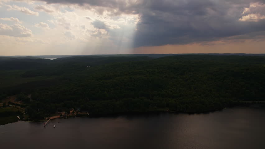Epic aerial shot of thick clouds and sunlight rays shoot down to the wild forest near Baptist Lake. Picturesque view of natural event, evening, Bancroft, Ontario, Canada.