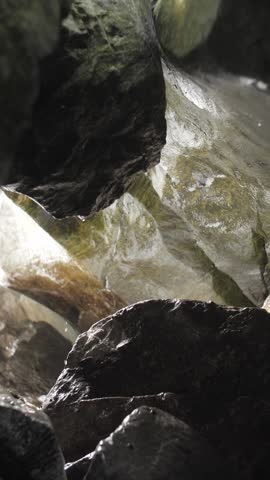 The sea waves crash against the rocks in the cave and turn into splashes and foam. Vertical format.