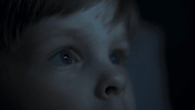 Close-up of a little boys face, lit by the blue light of the cinema screen, with a reflection in his eyes, as he watches intently and curiously at the movie on the TV, tablet, or plays computer games  - Powered by Shutterstock - Get 15% off with code: PIKWIZARD15