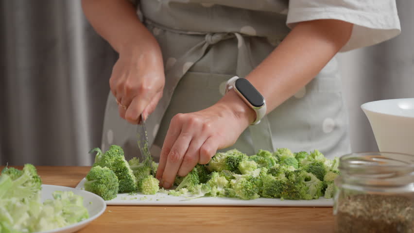 Meal prep process with fresh vegetables. A woman is chopping broccoli on a cutting board for a healthy recipe. The concept of diet planning, homemade food and batch cooking for the week.