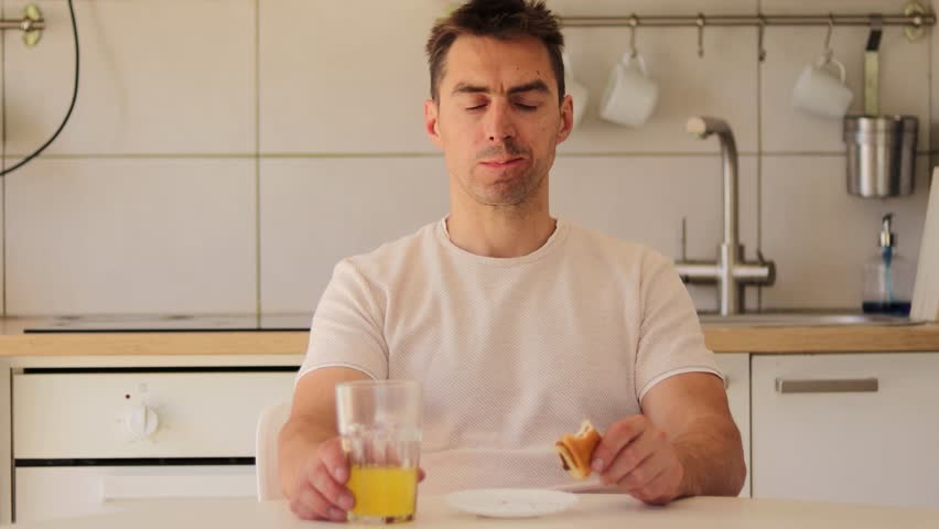 A man indulges in delicious cinnamon buns while savoring a glass of orange juice. This moment takes place in a bright, contemporary kitchen filled with light.
