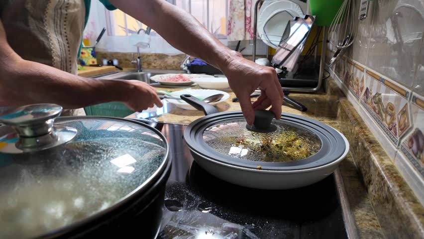 Mature professional chef preparing homemade Italian lunch, mixing zucchini, ham, and potatoes in kitchen pan while cooking pasta alongside