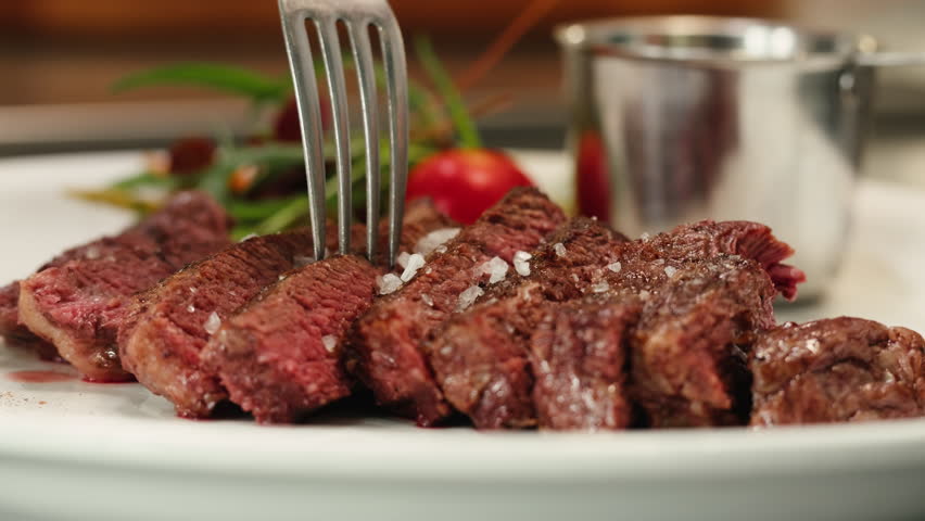 Beef angus steak in restaurant, close up Pieces of hot ribeye steak served on the wooden board. Medium steak slices with blood, salt and pepper in fancy meat cafe. 