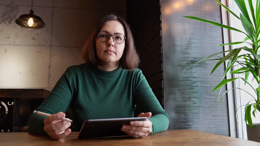 Pretty woman sitting in cafe and working. Green dress with long sleeves. Casual lifestyle portrait. Business female person draw with pencil. Vlog slow video. Wide