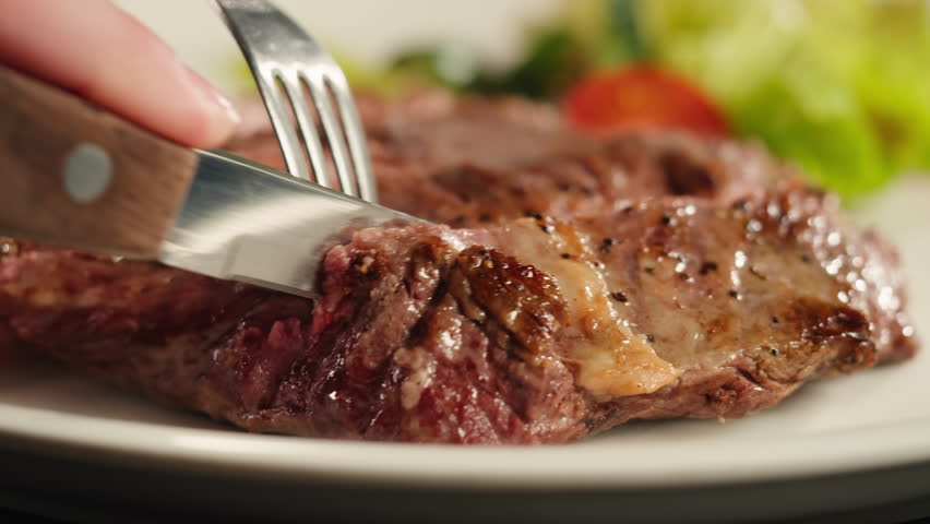 Beef angus steak in restaurant, close up Pieces of hot ribeye steak served on the wooden board. Medium steak slices with blood, salt and pepper in fancy meat cafe. 