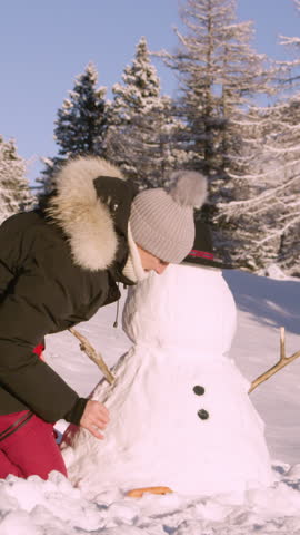 SLOW MOTION, CLOSE UP: Cheerful young woman is building a snowman on a sunny winter day. Caucasian female tourist enjoys a fun day outdoors by making a snowman. Woman is putting buttons on a snowman.