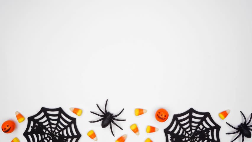 Halloween bottom border of scattered candy and spider webs. Above view stop motion loop video over a white background with copy space.