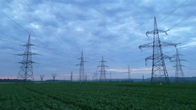 Electricity pylons traverse a vast agricultural landscape under twilight, symbolizing sustainable energy. A dolly shot captures the blend of rural fields and modern power transmission. - Powered by Shutterstock - Get 15% off with code: PIKWIZARD15