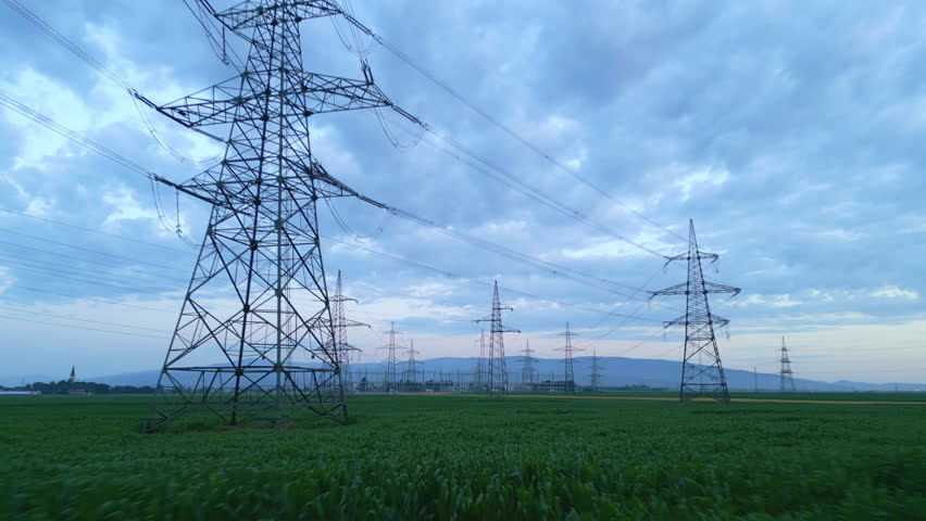Panoramic view of an expansive electrical grid with tall pylons over a verdant field under a dramatic sky, showcasing sustainable energy infrastructure blending nature and modern power transmission.
