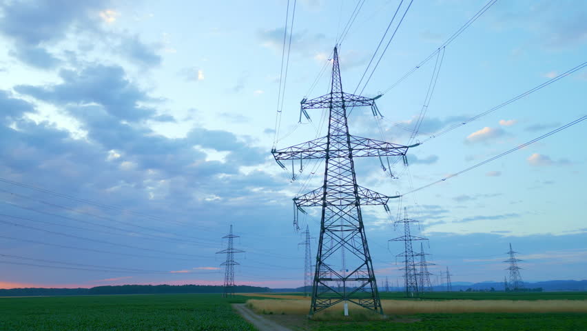 Power lines stretch across a serene sunset landscape, with silhouetted electricity pylons against a vibrant sky, symbolizing sustainable energy infrastructure and modern power distribution.