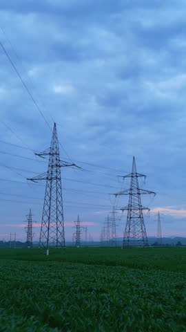 Establishing shot of electricity pylons in a lush green field under twilight, symbolizing sustainable energy infrastructure. Harmony between industrial power lines and nature.