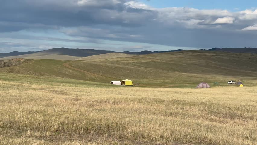 Video of landscape of coast of Lake Baikal on August day. Steppe meadows and hills of Olkhon Island on summer afternoon. In the distance, tent camp of tourists. Natural background. Summer travel and r
