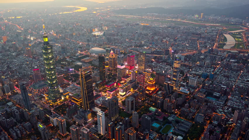 Aerial hyperlapse of Downtown Taipei at dusk, the vibrant capital city of Taiwan, with 101 Tower standing out amid skyscrapers in XinYi Commercial District and city lights dazzling under twilight sky