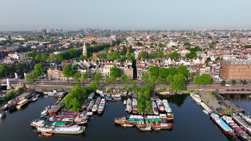 Scenic drone shot of Amsterdam with the historic Montelbaanstoren tower, canals, and Dutch rooftops.
