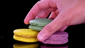 Hand selects pastel macarons from glossy black surface, showcasing vibrant colors, texture, and arrangement. - Powered by Shutterstock - Get 15% off with code: PIKWIZARD15
