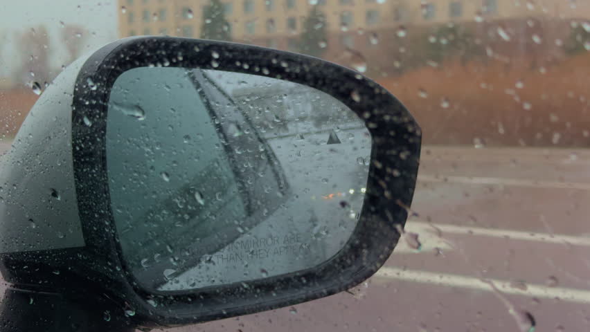Driving car on highway road on rainy weather with strong wind. Side view from the front passenger side with BSM alert on the side mirror. Close up