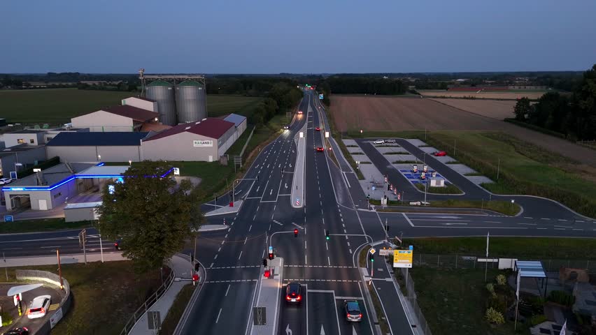 New build industrial district of German town st dusk. Electric vehicle charging station, silo storage factories, gas stations and mc Donalds restaurant. Aerial forward wide shot.