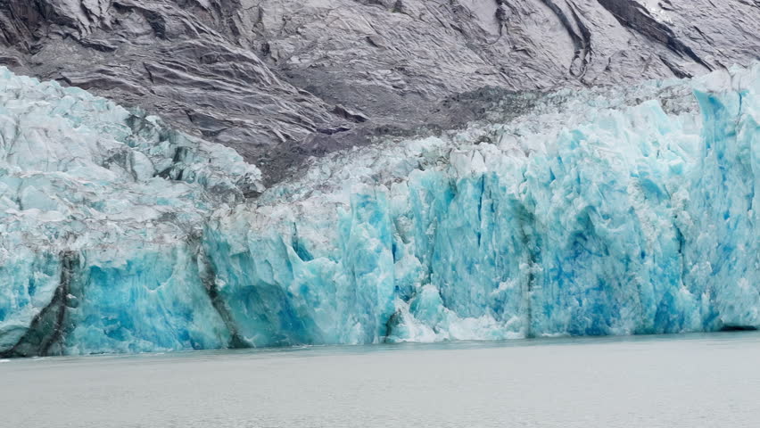 This is a close-up shot of a piece of the blue ice wall calving off the Dawes Glacier in Endicott Arm near Juneau Alaska. It shows white seagulls flying around showing scale.