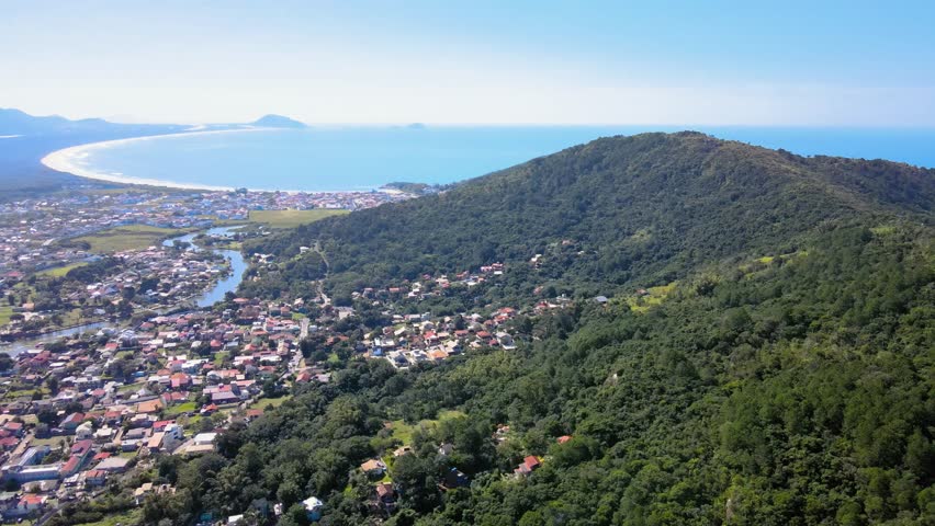 Aerial panoramic drone view of Barra da Lagoa, an urbanized neighborhood with a freshwater canal running through the city that flows into the sea, Florianópolis, Santa Catarina, Brazil.