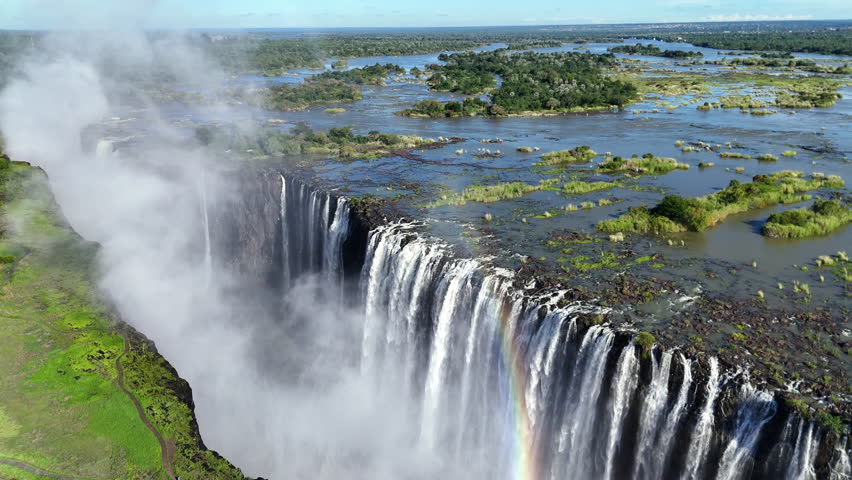 Aerial view of Victoria Falls with powerful waterfall plunging into gorge, mist rising above lush green forest, dramatic natural wonder and iconic travel destination in Africa