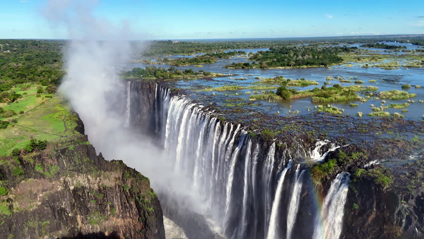 Aerial view of Victoria Falls with powerful waterfall plunging into gorge, mist rising above lush green forest, dramatic natural wonder and iconic travel destination in Africa