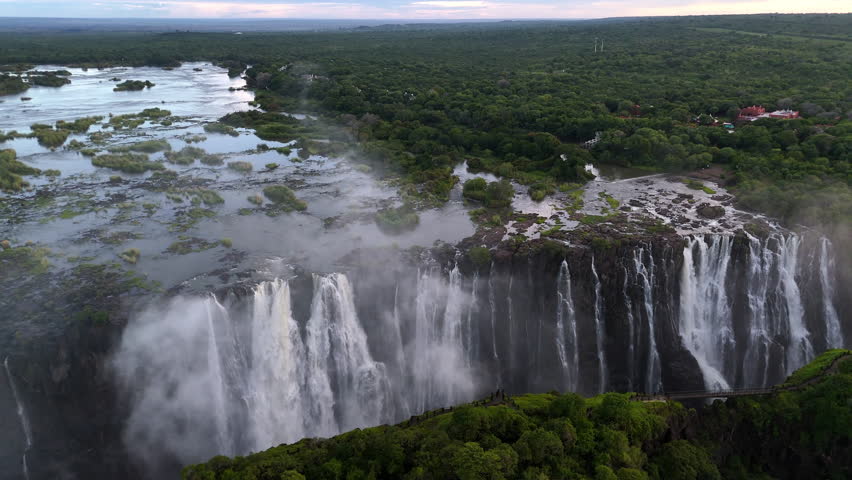 Aerial view of Victoria Falls with powerful waterfall plunging into gorge, mist rising above lush green forest, dramatic natural wonder and iconic travel destination in Africa