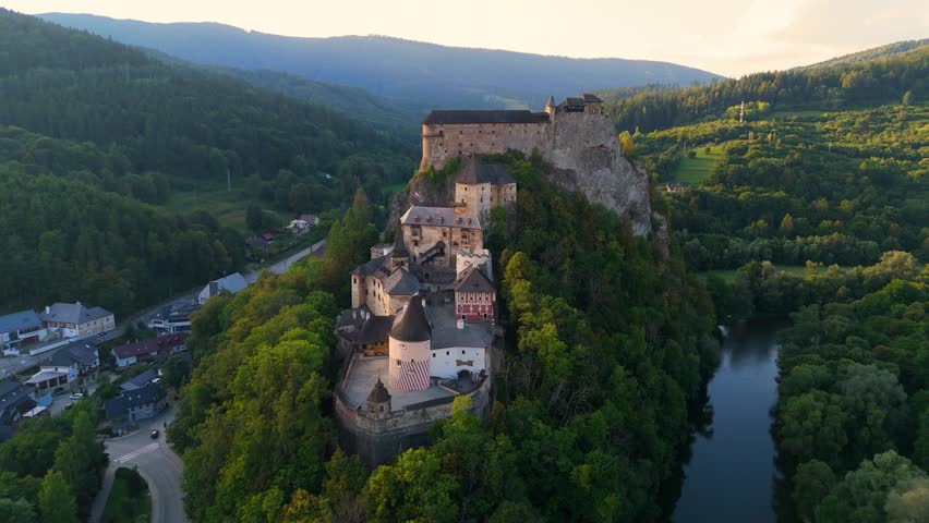 Drone footage of Orava Castle perched on dramatic cliffs above the Orava River in Slovakia. Sunset light reveals medieval architecture and breathtaking landscape. Ideal for history and travel visuals.