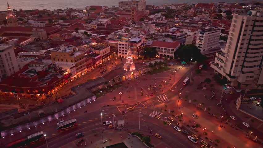 Aerial tilt down shot of plaza de la independencia at dusk, showcasing illuminated clock tower and surrounding colonial architecture, cartagena de indias, colombia