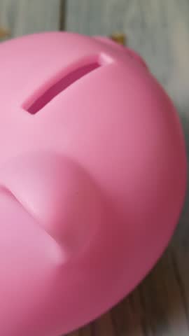 An unrecognizable hand puts coins in a piggy bank in the form of a pink pig. Home budget, money savings and financial planning concept