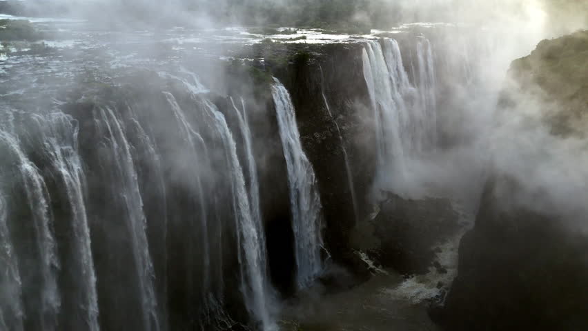 Aerial view of Victoria Falls with powerful waterfall plunging into gorge, mist rising above lush green forest, dramatic natural wonder and iconic travel destination in Africa