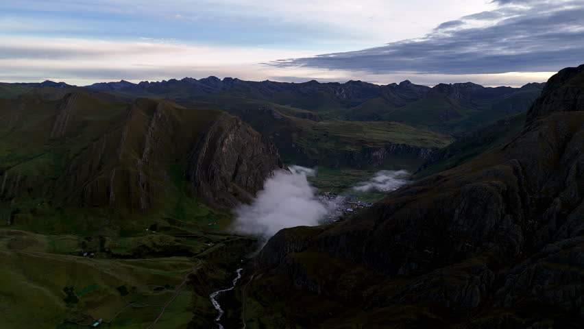 Cinematic aerial view of snowy Andes mountains in Peru with glaciers, rocky cliffs, and hidden blue alpine lake under misty clouds, dramatic landscape and natural travel destination
