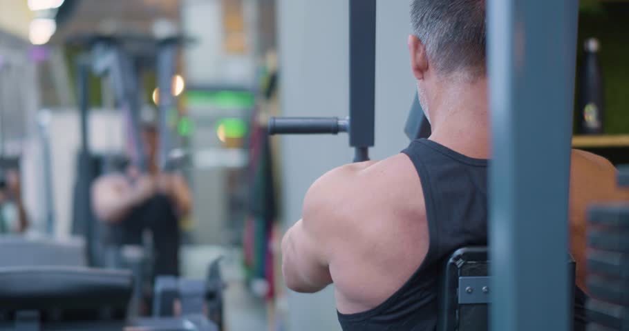 Gym workout. Butterfly exercise. Back view of a middle aged Caucasian man trains chest in the gym. Gym workout shows man targeting pectorals through butterfly machine exercise.
