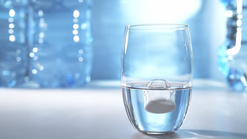 Effervescent tablet falling into glass of water on blue background. Acetylsalicylic acid painkiller tablet. Aspirin effervescent pill in water.