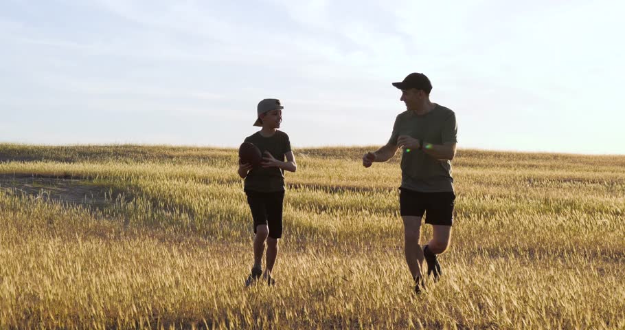 happy child playing american football with dad. joyful child spends holidays playing american football. dad and son run on golden field throwing ball each other. active games of children and parents.