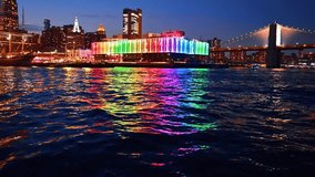 Beautiful rainbow illumination of Pier 17 Bar reflecting in the dark riverscape. River cruise approaching the Brooklyn Bridge at night. New York, USA. - Powered by Shutterstock - Get 15% off with code: PIKWIZARD15