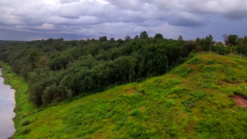 Tranquil riverside view showing lush greenery and dramatic skies in a serene natural setting from a moving train