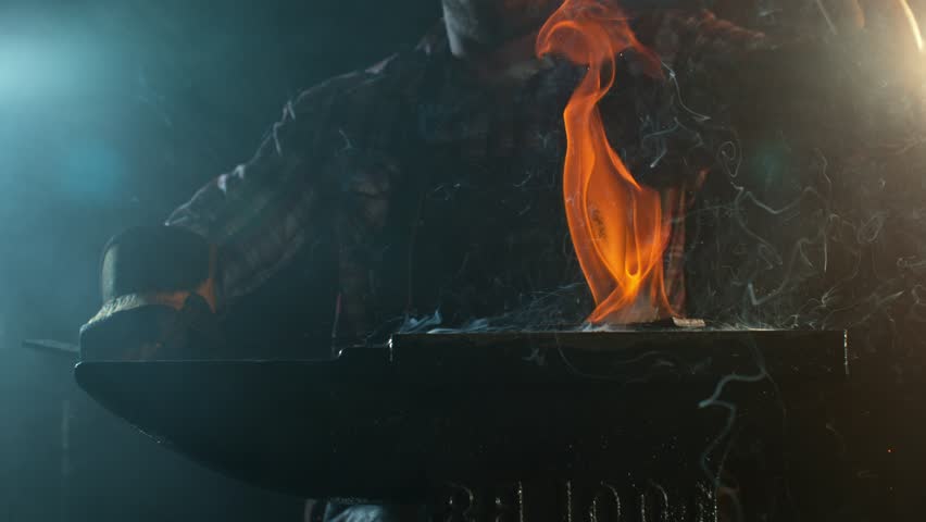 Close-up of blacksmith forging glowing hot iron on anvil with flying sparks. Super slow motion filmed on high-speed cinema camera at 1000 fps